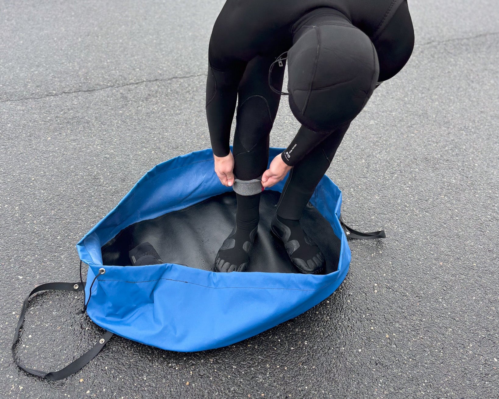 Surfer changing at the beach with a blue Clamshell Bag