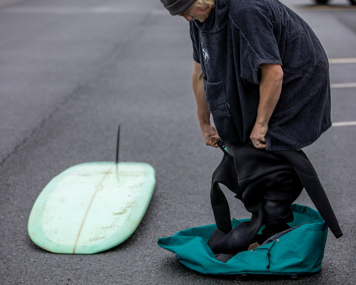 Surfer changing into a wetsuit at the beach using the clamshell wetsuit changing mat and wetsuit bag